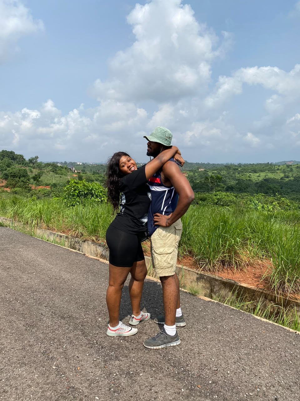 Nnenna wrapping her arms around Chukwuma on a road above green hills