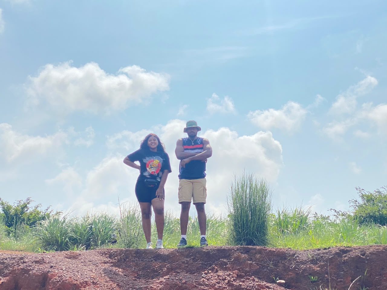 Nnenna and Chukwuma standing on a red earth ridge against a blue sky