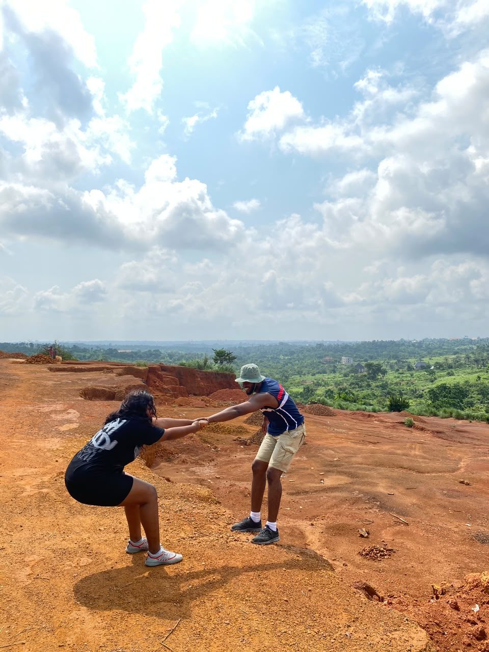 Chukwuma and Nnenna holding hands on red earth with a valley behind